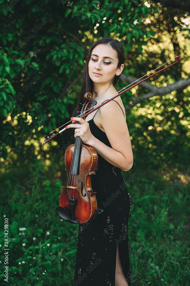 Beautiful girl with dark hair holds an old violin in her hands. Violinist