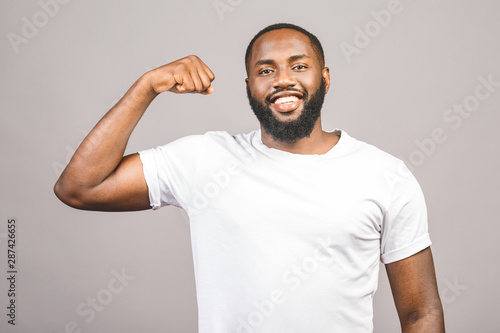 Close up portrait of a happy young african american man flexing bicep muscle isolated against grey background.