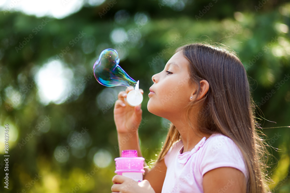 Children girl blowing soap bubbles outdoor