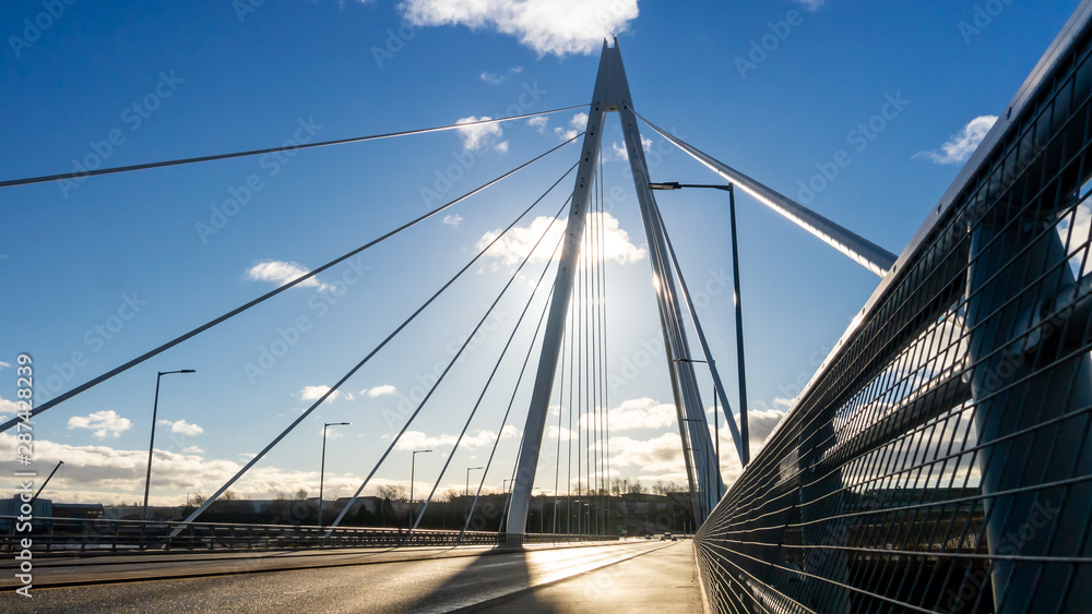 Naklejka premium Northern Spire Bridge (opened Summer 2018) in Sunderland spanning the River Wear. Photo taken facing the sun giving the bridge a silhouette contrasting with the blue sky with dark and white clouds.