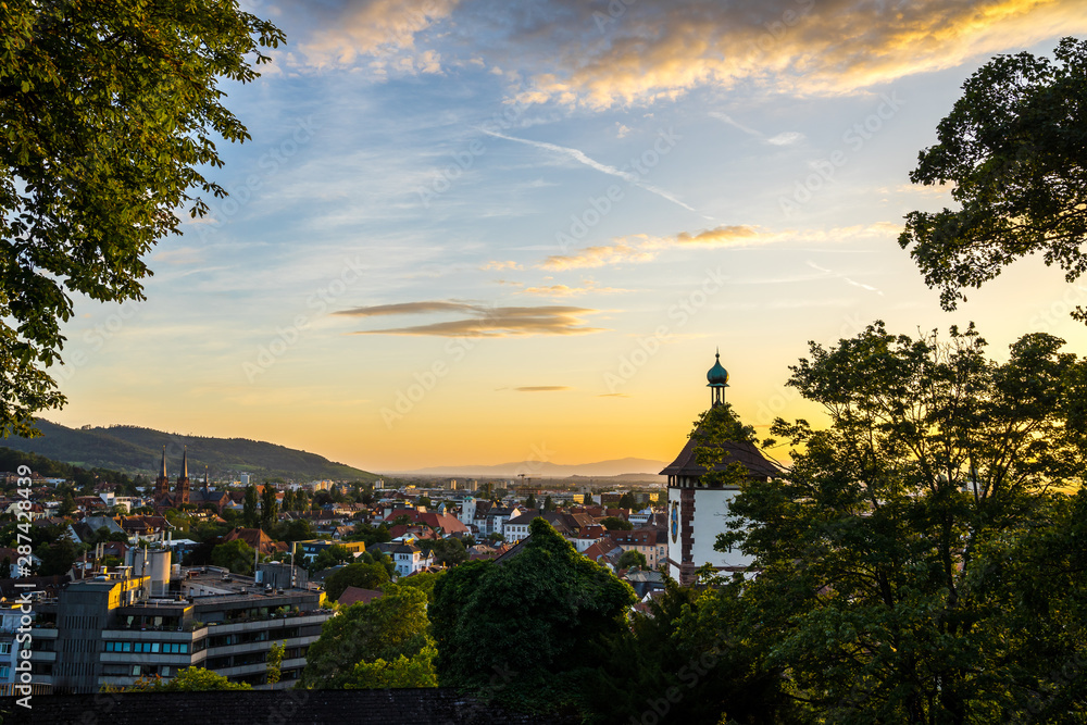 Germany, Beautiful warm sunset light shining on famous old city gate schwabentor in freiburg im breisgau, seen from above skyline of the city in summer with glowing sky