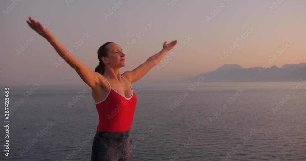 Caucasian woman in red relaxing by practicing yoga on the cliff near calm sea at sunset. Slow motion Caucasian woman in red relaxing by practicing yoga on the cliff near calm sea at sunset. Slow motion