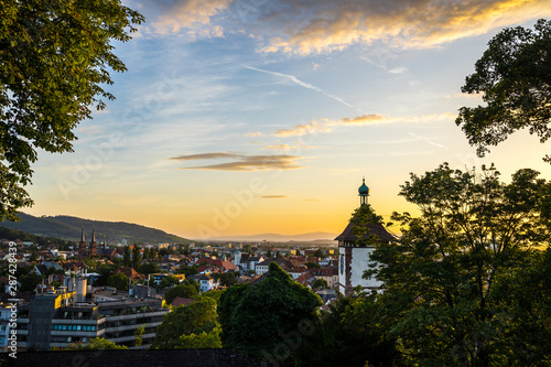 Germany, Beautiful warm sunset light shining on famous old city gate schwabentor in freiburg im breisgau, seen from above skyline of the city in summer with glowing sky © Simon