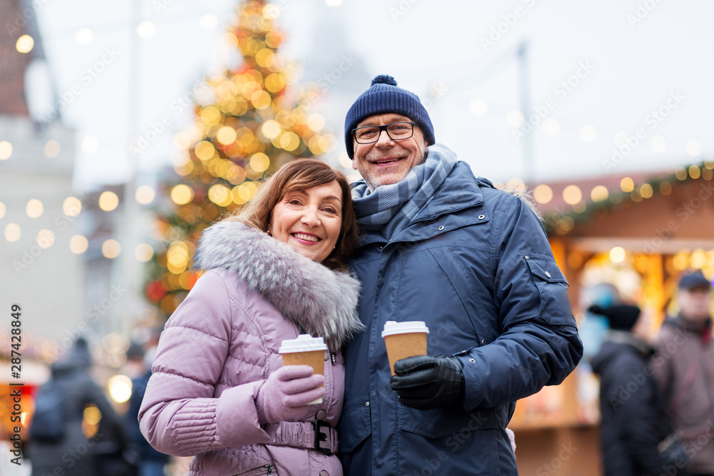 love, winter holidays and people concept - happy senior couple with takeaway coffee at christmas market on town hall square in tallinn, estonia