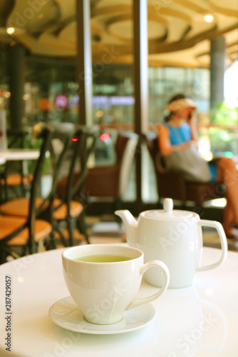 Vertical image of a white cup and teapot of green tea served on cafe's white table