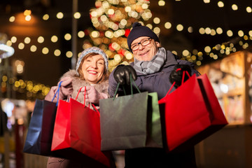 sale, winter holidays and people concept - happy senior couple with shopping bags at christmas market souvenir shop on town hall square in tallinn, estonia