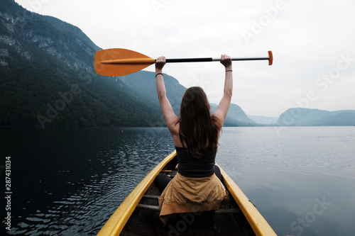 Young woman canoeing in the lake bohinj on a summer day, background alps mountains.