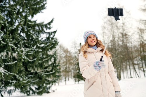 people, season and leisure concept - happy smiling woman taking picture by selfie stick in winter