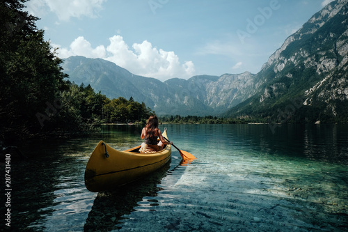 Young woman canoeing in the lake bohinj on a summer day, background alps mountains.