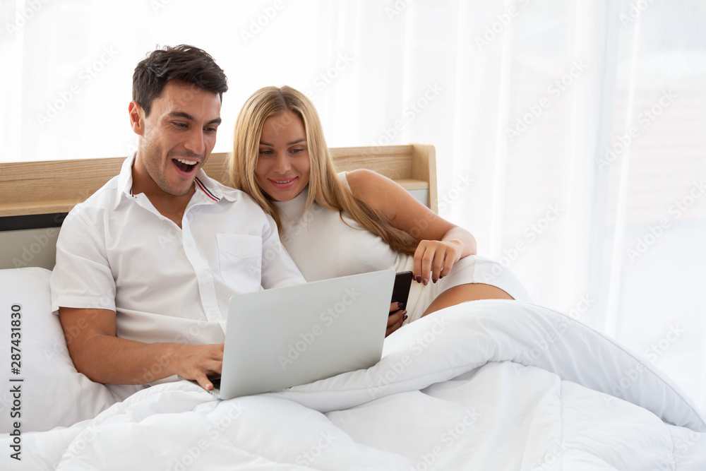 Caucasian couple searching cheap flight ticket and hotel in web online with laptop on bed, Preparing and find amazing accommodations for holidays concept Caucasian couple searching cheap flight ticket and hotel in web online with laptop on bed, Preparing and find amazing accommodations for holidays concept
