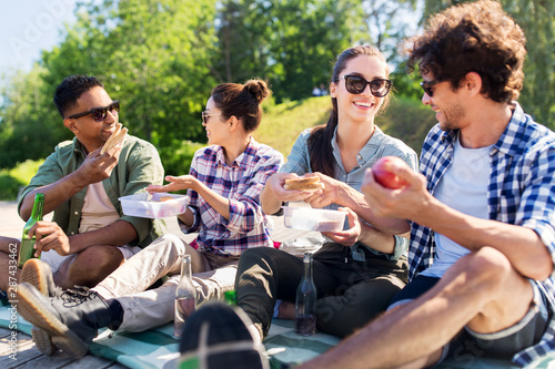 leisure and people concept - group of happy friends having picnic and eating sandwiches at summer park