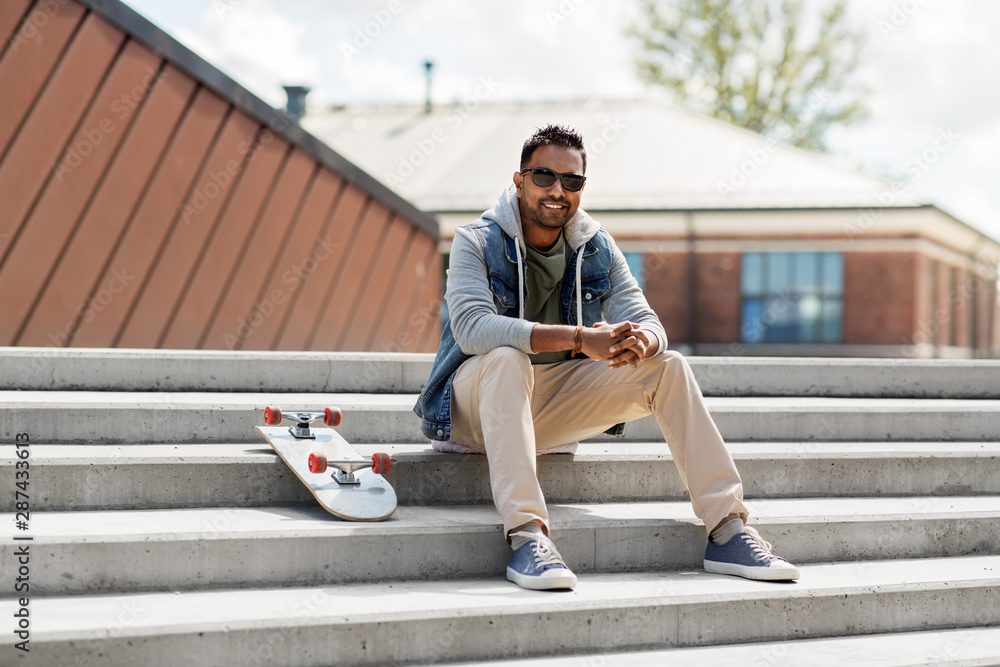people and leisure concept - smiling indian man with skateboard sitting on stairs on city roof top people and leisure concept - smiling indian man with skateboard sitting on stairs on city roof top