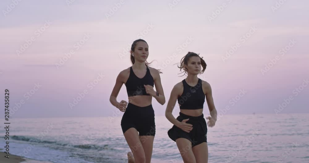 Beautiful two ladies running on the beach side concentrated enjoying the moment in the morning practicing sport. slow motions Beautiful two ladies running on the beach side concentrated enjoying the moment in the morning practicing sport. slow motions