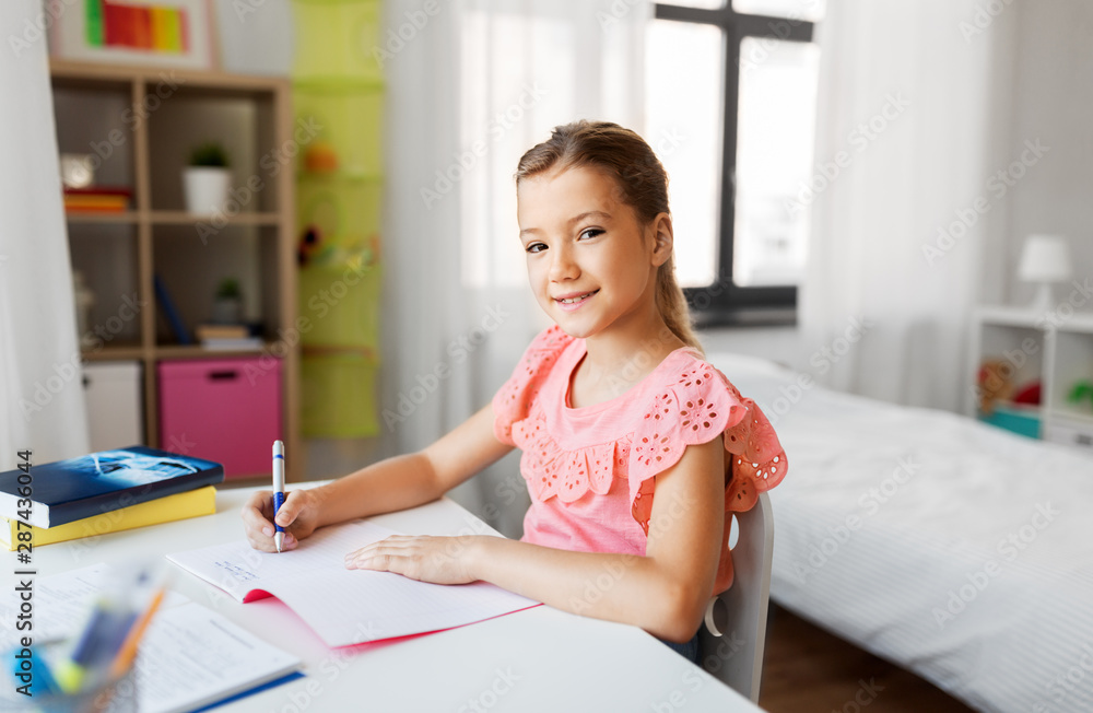 children, education and learning concept - student girl with book writing to notebook at home