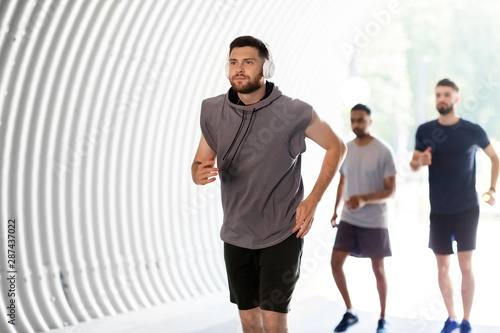 fitness, sport and healthy lifestyle concept - young men or male friends with headphones running outdoors