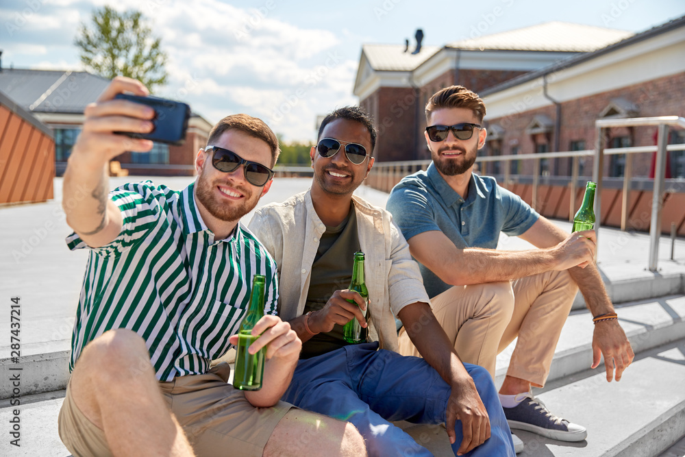 leisure, technology and people concept - happy male friends taking selfie by smartphone and drinking beer on street in summer