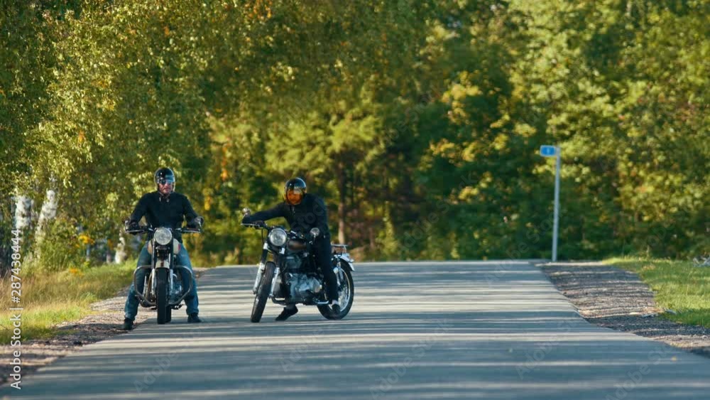 Two brutal men motorcyclists standing on the road by each other and getting ready for the race Two brutal men motorcyclists standing on the road by each other and getting ready for the race