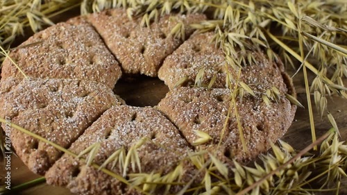 Fresh round oat bread and oat ears of grain rotating on brown wooden table. Stomach friendly food.