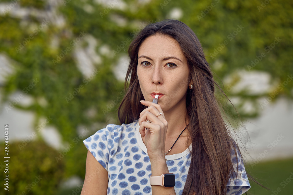 Electronic cigarette technology. Tobacco IQOS system. Close-up of a girl smoking an electric hybrid cigarette with a heating pad. tobacco heating system. Electronic cigarette in female hands. Electronic cigarette technology. Tobacco IQOS system. Close-up of a girl smoking an electric hybrid cigarette with a heating pad. tobacco heating system. Electronic cigarette in female hands.