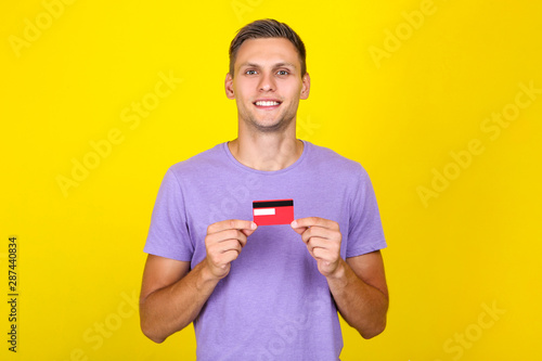 Young man holding credit card on yellow background