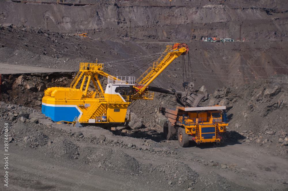 mining machinery works in a quarry. excavator loads a dump truck, heavy trucks transport iron ore. open pit mining mining machinery works in a quarry. excavator loads a dump truck, heavy trucks transport iron ore. open pit mining