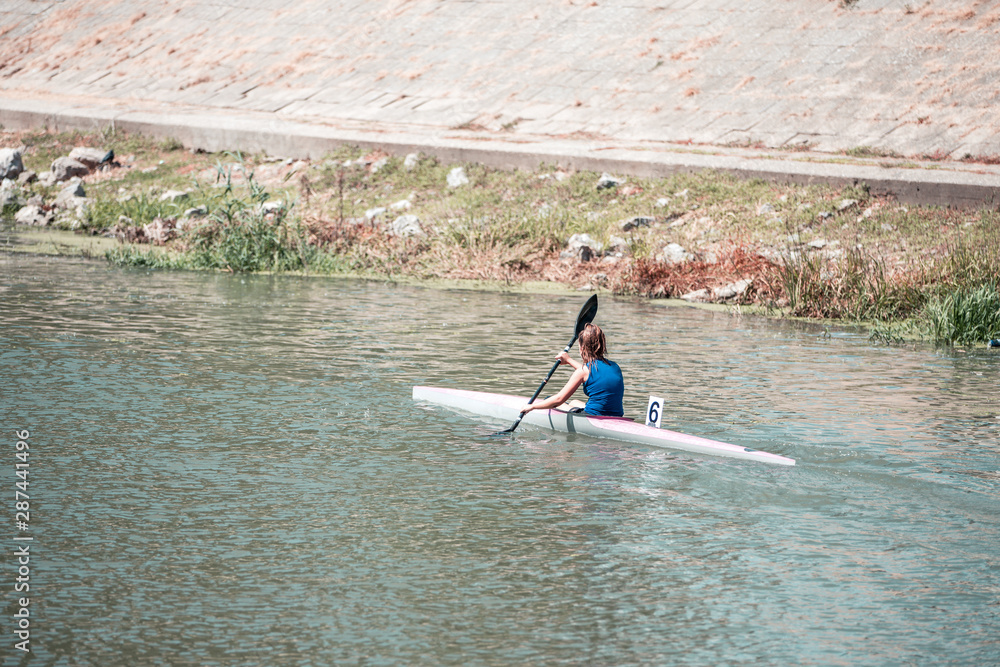 Young woman on rowing kayak on lake during competition