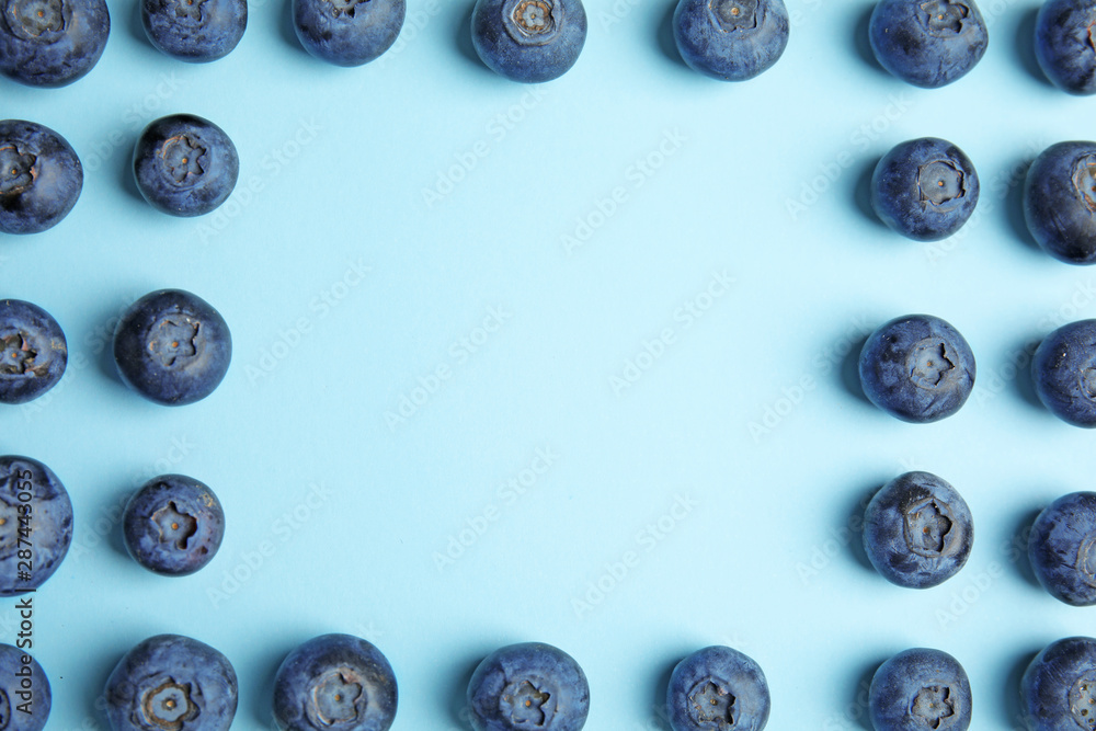 Frame of ripe blueberries on blue background, flat lay with space for text