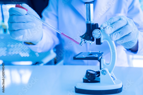 A Scientist are working in the laboratory.,A students are testing in the classroom. A young scientist drops red water from a glass tube on a microscope in a laboratory.