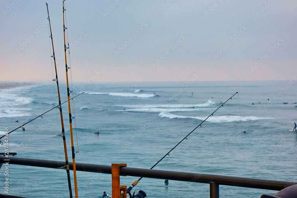 Fishing poles on a pier with the surf in the background.