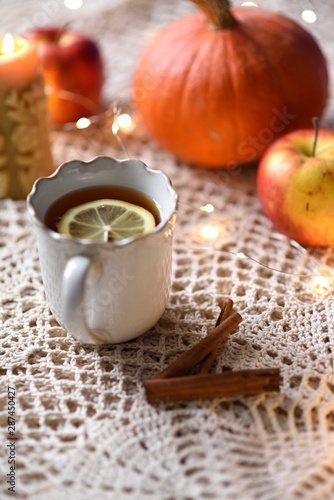 Cup of warm tea with lemon with pumpkins, apples, candle and spices, fall scene