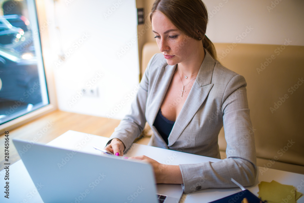 Business woman online banking via mobile phone during work on laptop computer during break in restaurant. Female marketer sending sms via cell telephone after webinar on netbook device Business woman online banking via mobile phone during work on laptop computer during break in restaurant. Female marketer sending sms via cell telephone after webinar on netbook device