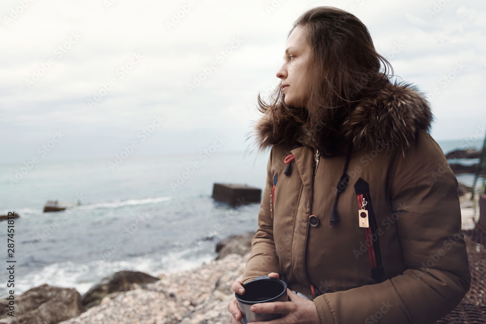 Smiling beautiful young woman standing on sea coast during cloudy weather