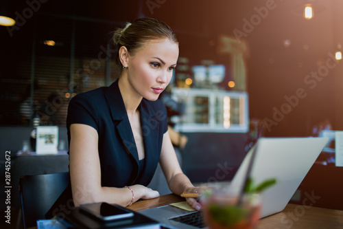 Woman professional economist checking e-mail on laptop computer while sitting in restaurant during work break in company. Female experienced business writer for executive summary using netbook