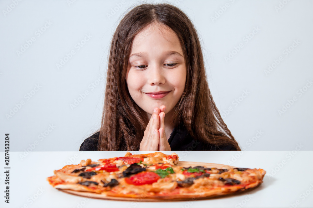 The little girl looks at the pizza. The child prays before eating The little girl looks at the pizza. The child prays before eating