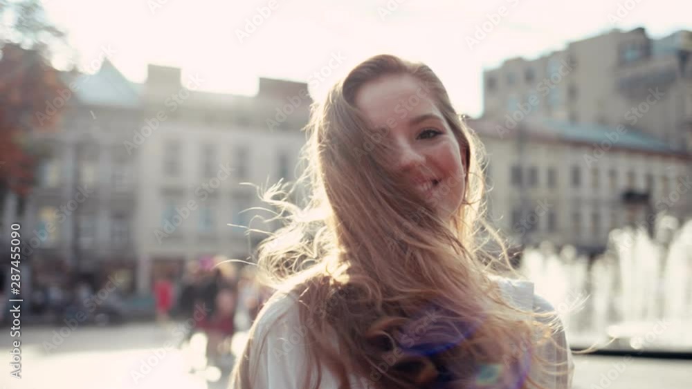 Sunshine young smiling woman with curly hair returns look at camera smile walking in the city streets portrait happy summer face sunset beautiful lady outdoor close up slow motion