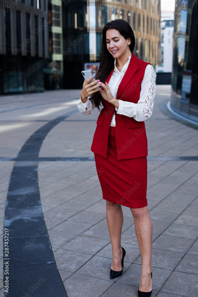 Fototapeta premium Happy smiling luxury business woman reading good news in e-mail on smartphone while standing outdoors near contemporary office buildings. Joyful female leadership online banking via cellphone