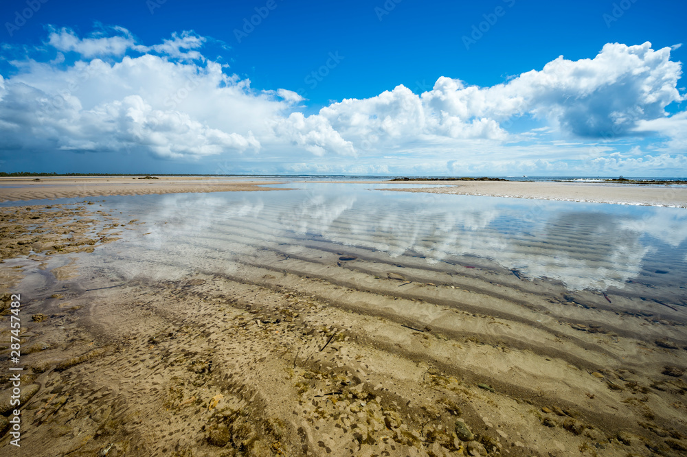 Scenic background of calm waters reflecting tropical clouds on the deserted shore of a remote island beach in Bahia, Brazil
