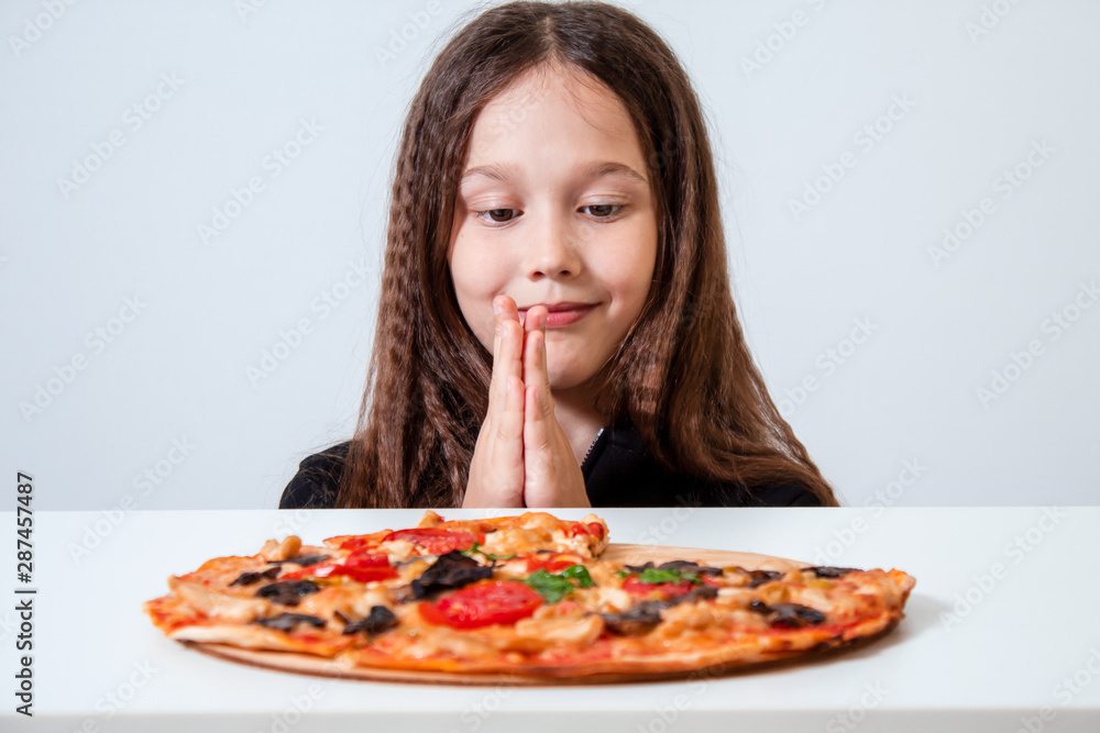 The little girl looks at the pizza. The child prays before eating