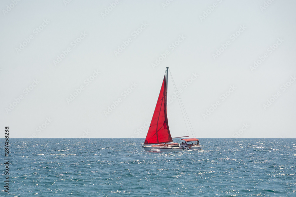Red sail boat floating in sunny day