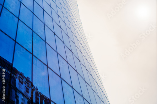 Bottom view of a modern skyscraper building with glass window against sky background for promotional content. Contemporary business centre with new perspective design