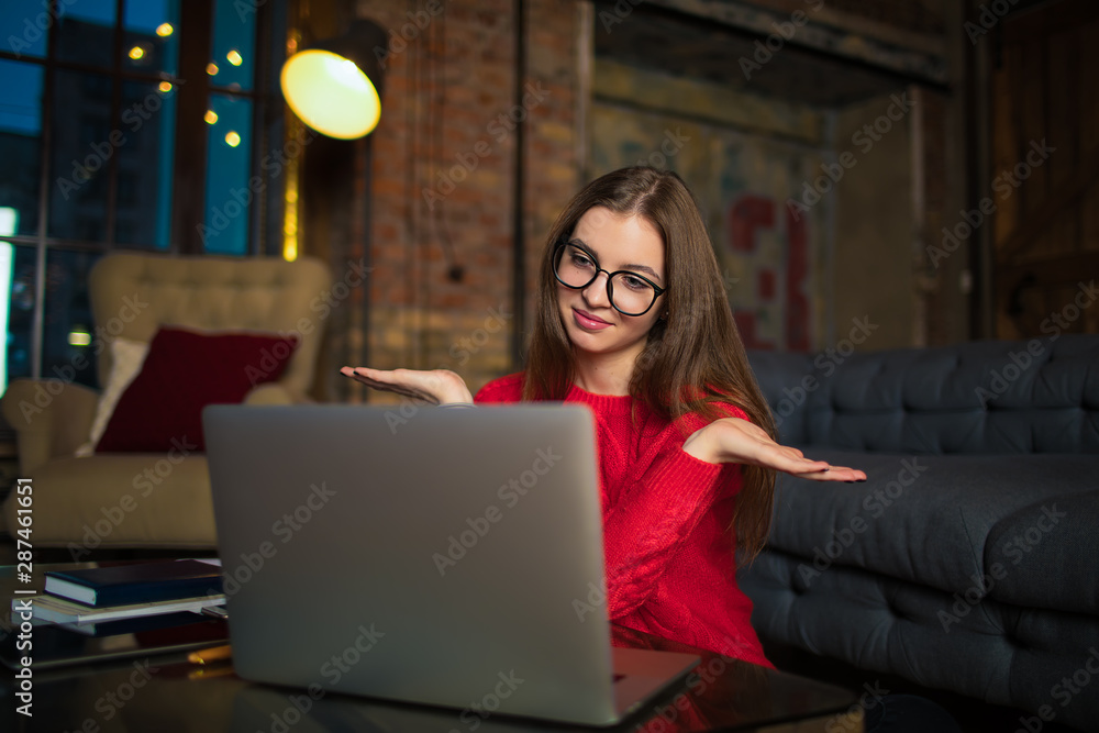 Pretty woman in glasses skilled freelance worker having video conference via laptop computer, sitting indoors home interior. Female blogger having online call via notebook, don't know gesture Pretty woman in glasses skilled freelance worker having video conference via laptop computer, sitting indoors home interior. Female blogger having online call via notebook, don't know gesture