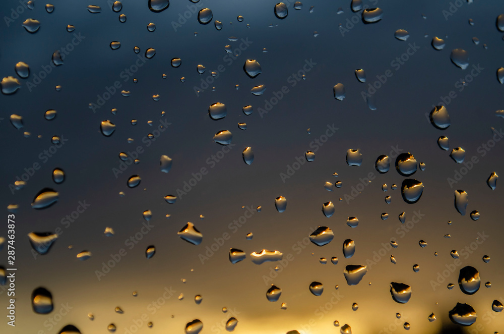 Rain outside window on background of sunset. Rain drops on glass during rain. Bright texture of water drops