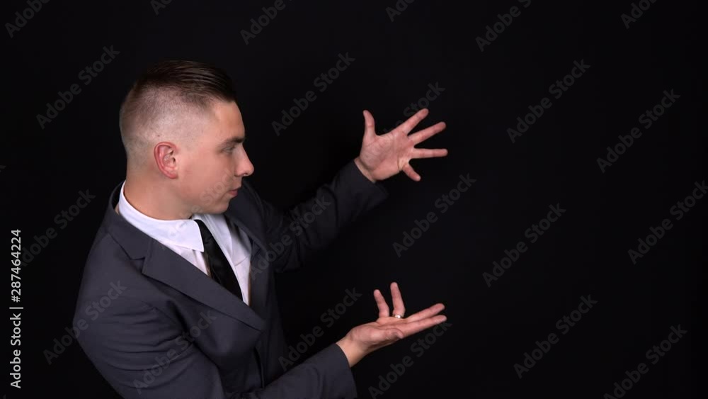 A young businessman points with their hands. Isolated black background A young businessman points with their hands. Isolated black background