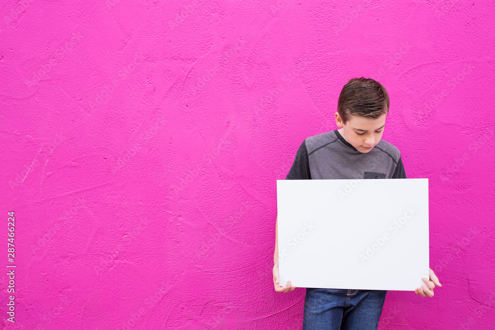 isolated cute boy holding blank white sign with space on colorful bright background isolated cute boy holding blank white sign with space on colorful bright background