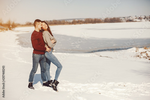 Cute couple have fun. Boy and girl in a winter park. Man in a red sweater. Brunette in a gray sweater. Loving couple walking around the ice © hetmanstock2