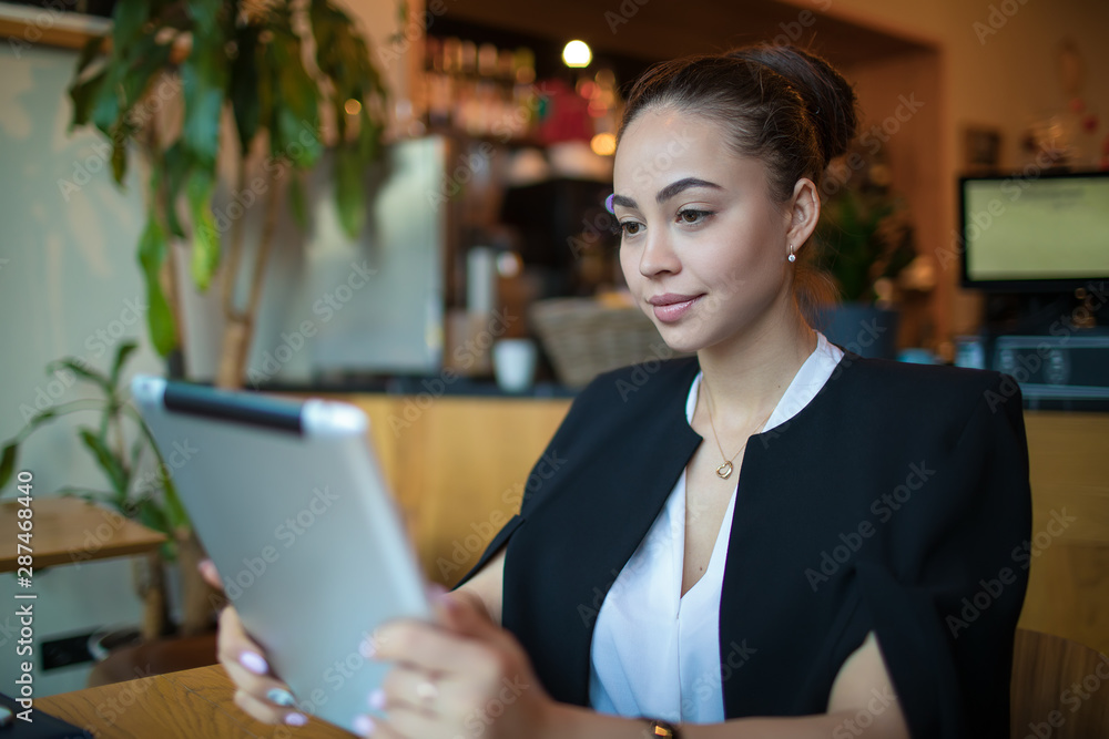 Young Caucasian female smart university student online learning via portable touch pad while sitting in coffee shop. Confident woman restaurant manager checking e-mail via digital gadget computer Young Caucasian female smart university student online learning via portable touch pad while sitting in coffee shop. Confident woman restaurant manager checking e-mail via digital gadget computer