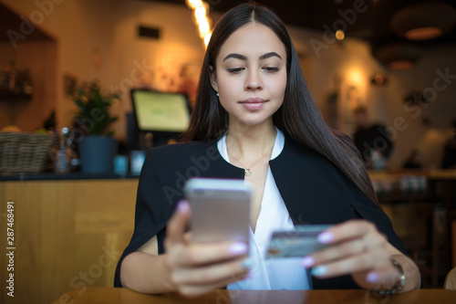 Confident business woman online payment via mobile phone using credit debit card while relaxing in restaurant. Female online shopping store via cellphone, resting in coffee shop during recreation time