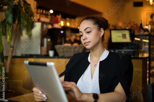 Woman skilled business owner online banking via portable touch pad computer while sitting in restaurant during work break. Female manager using application on digital tablet, resting in coffee shop