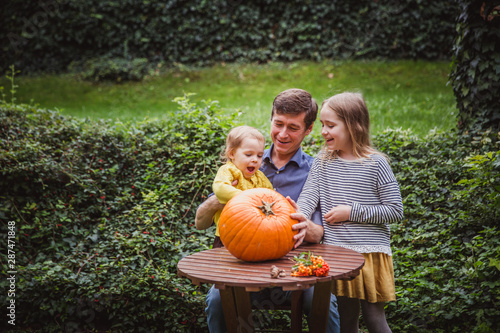 Happy halloween. Father and two daughters look at the face cut in the pumpkin for Halloween outside. © Evgeniya Biriukova