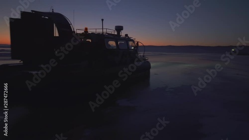 People in hovercraft moving on frozen Lake Baikal against sky during sunset